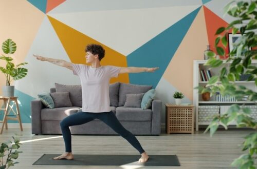 Person gör en stående stretchövning på en yogamatta i vardagsrummet